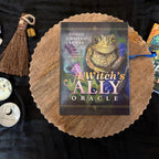 Book titled 'A Witch's Ally Oracle' on a wooden surface with mystical items around.