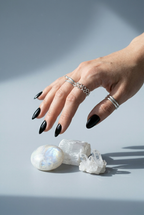 Hand with black nail polish wearing silver rings on a light gray background