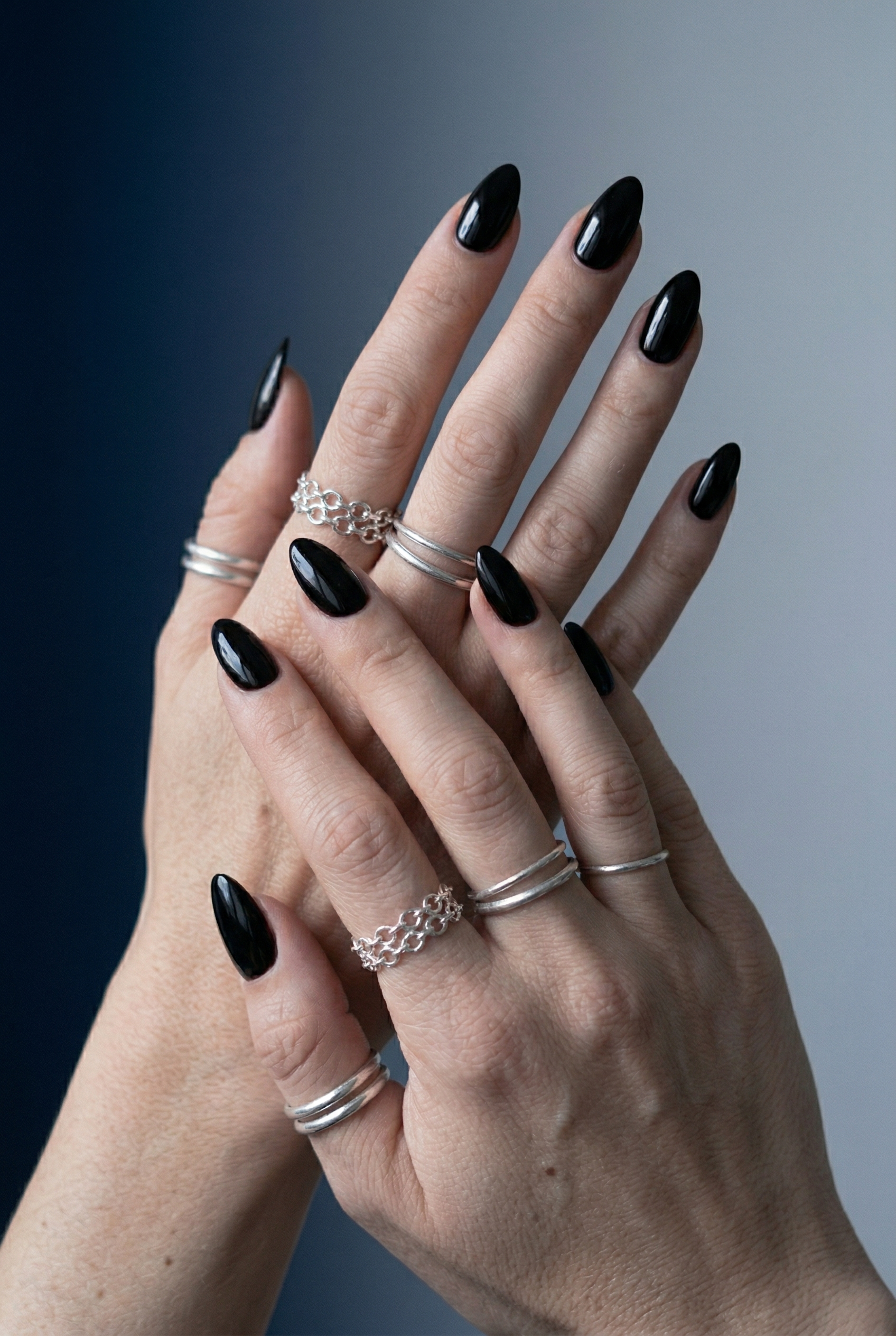 Close-up of hands with black nail polish and silver rings on a gradient background