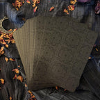Set of black playing cards with intricate design on a textured surface with dried flowers and a moon symbol.