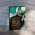 Book titled 'Ask the Feline Sages' with a cat illustration on the cover, placed on a textured surface.