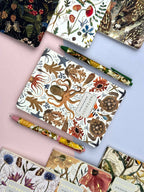 Notebooks with nature-themed designs and matching pencils on a colorful background