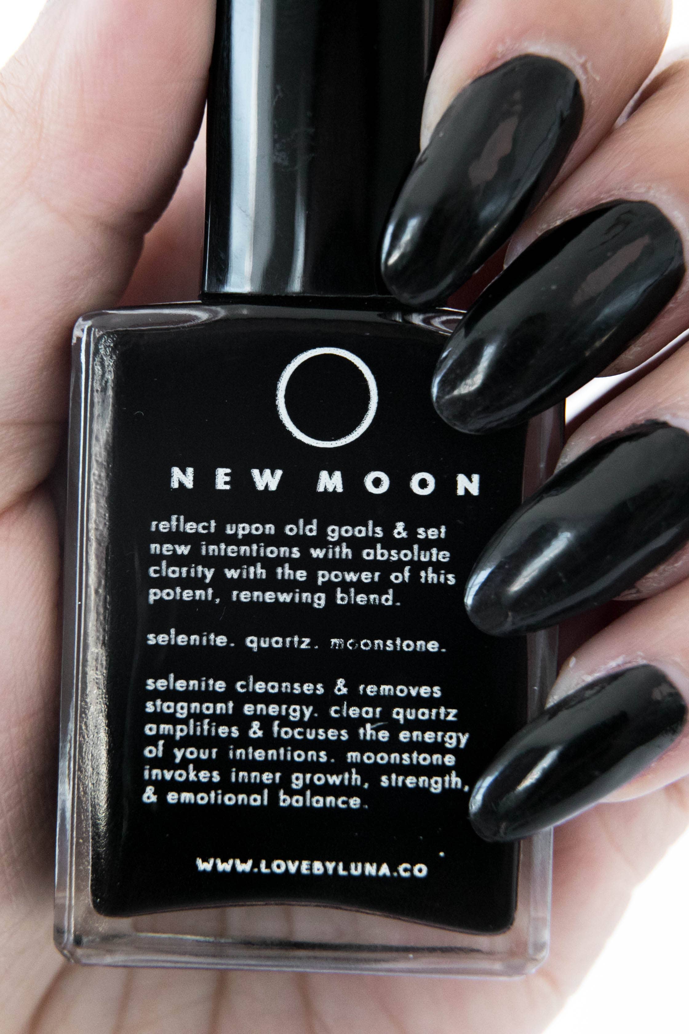Black nail polish bottle with text held by a hand with black nails on a white background