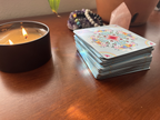 Stack of tarot cards next to a lit candle on a wooden surface