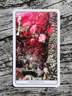 Tarot card titled 'Obsession' with a colorful design on a wooden surface
