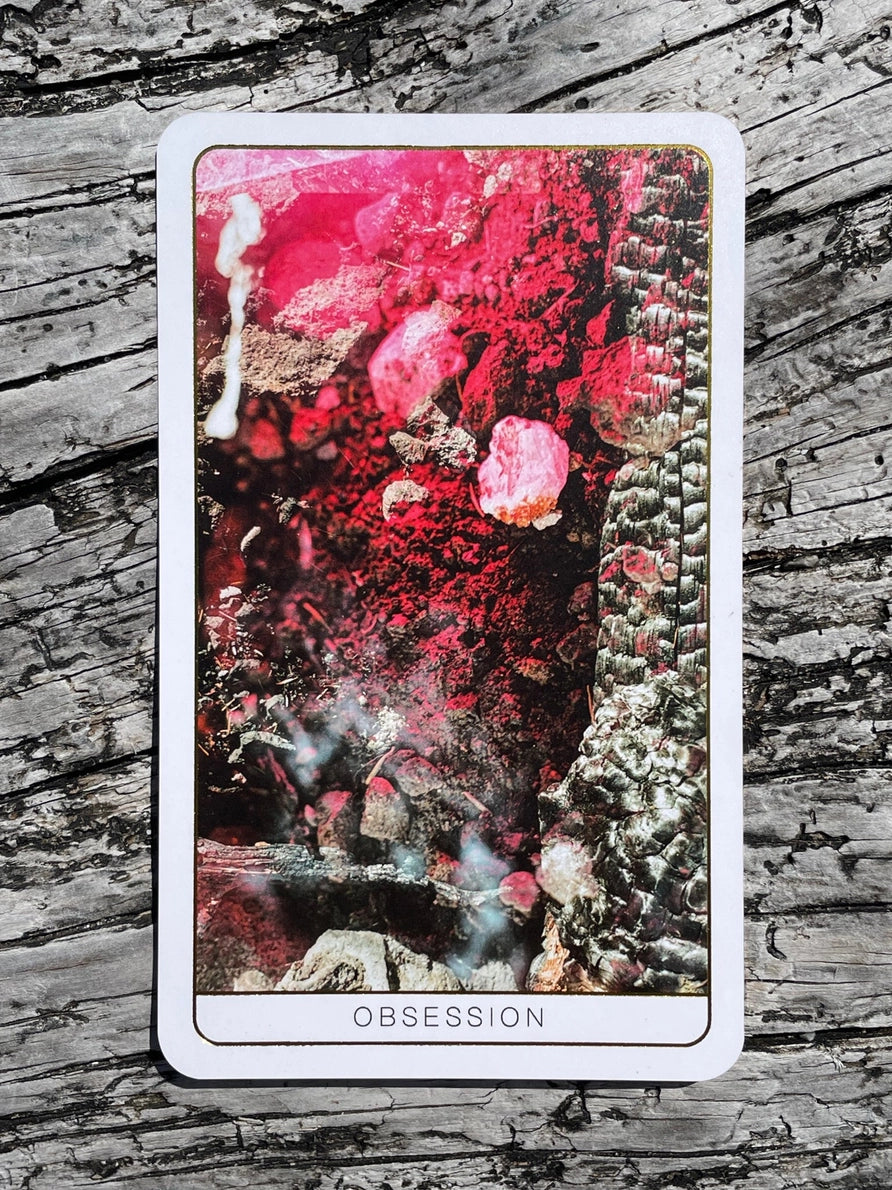 Tarot card titled 'Obsession' with a colorful design on a wooden surface