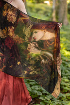 Person holding a large, intricately designed scarf with a floral and portrait pattern against a natural background.