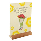 Decorative sign with a frog wearing a red mushroom hat and motivational quote on a yellow background.