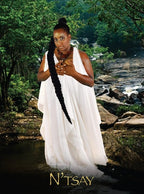 Woman in a white dress with a long black hair extension standing by a stream with 'N'TSAY' branding.