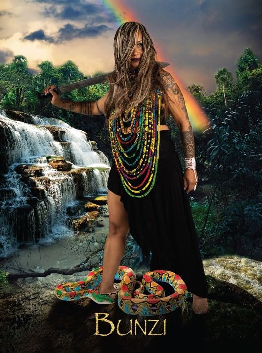 Woman with tattoos and colorful necklaces standing in front of a waterfall with a rainbow, wearing a black dress.