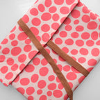Pink polka dot fabric with a brown strap on a light gray background