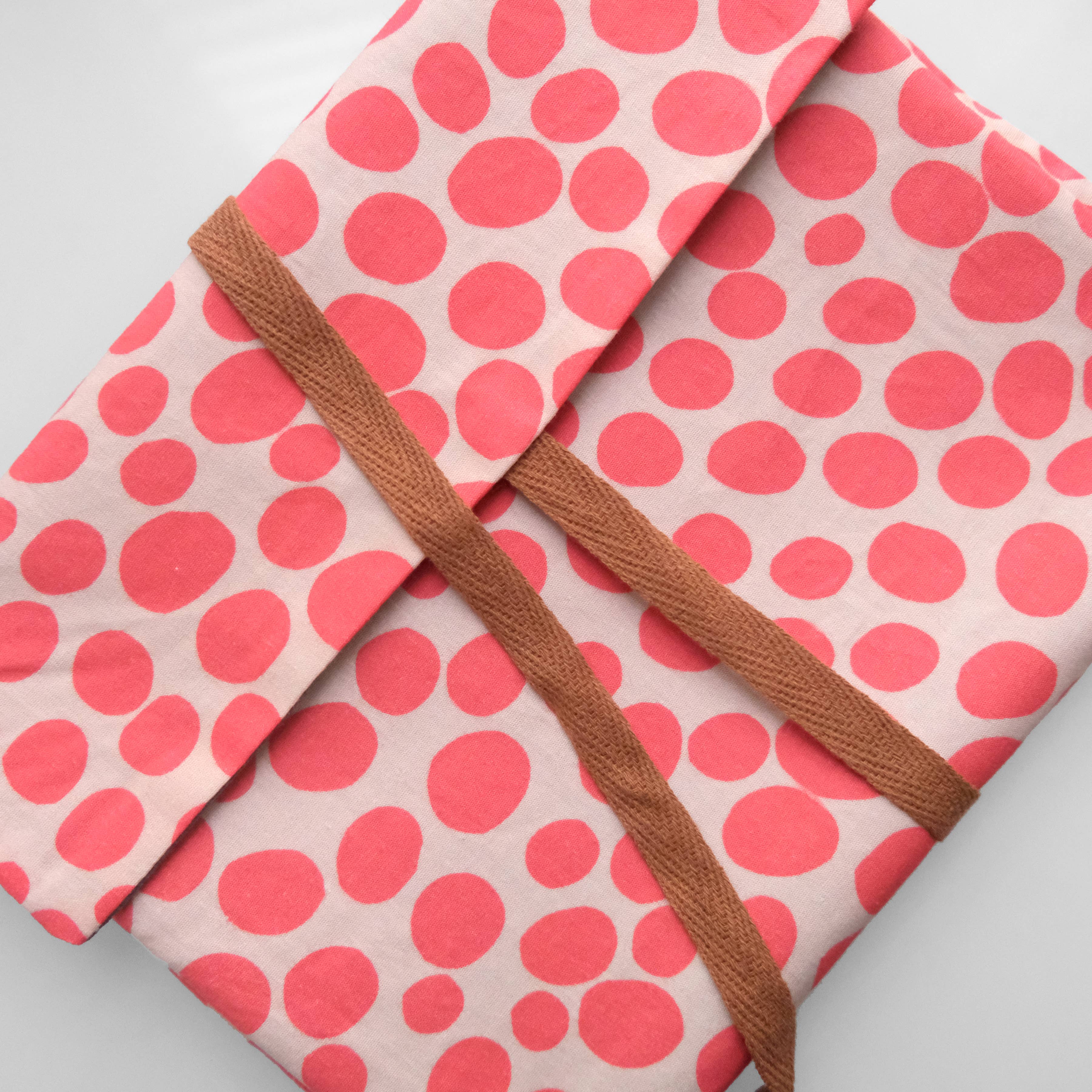 Pink polka dot fabric with a brown strap on a light gray background