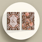 Two decorative greeting or blogging cards displayed upright on a round white surface against a warm beige background. The cards feature ornate floral and damask-style artwork in brown, blush pink, and beige tones, with one card showing a central label reading 'Bouchettes' and the other showing large pink flowers.