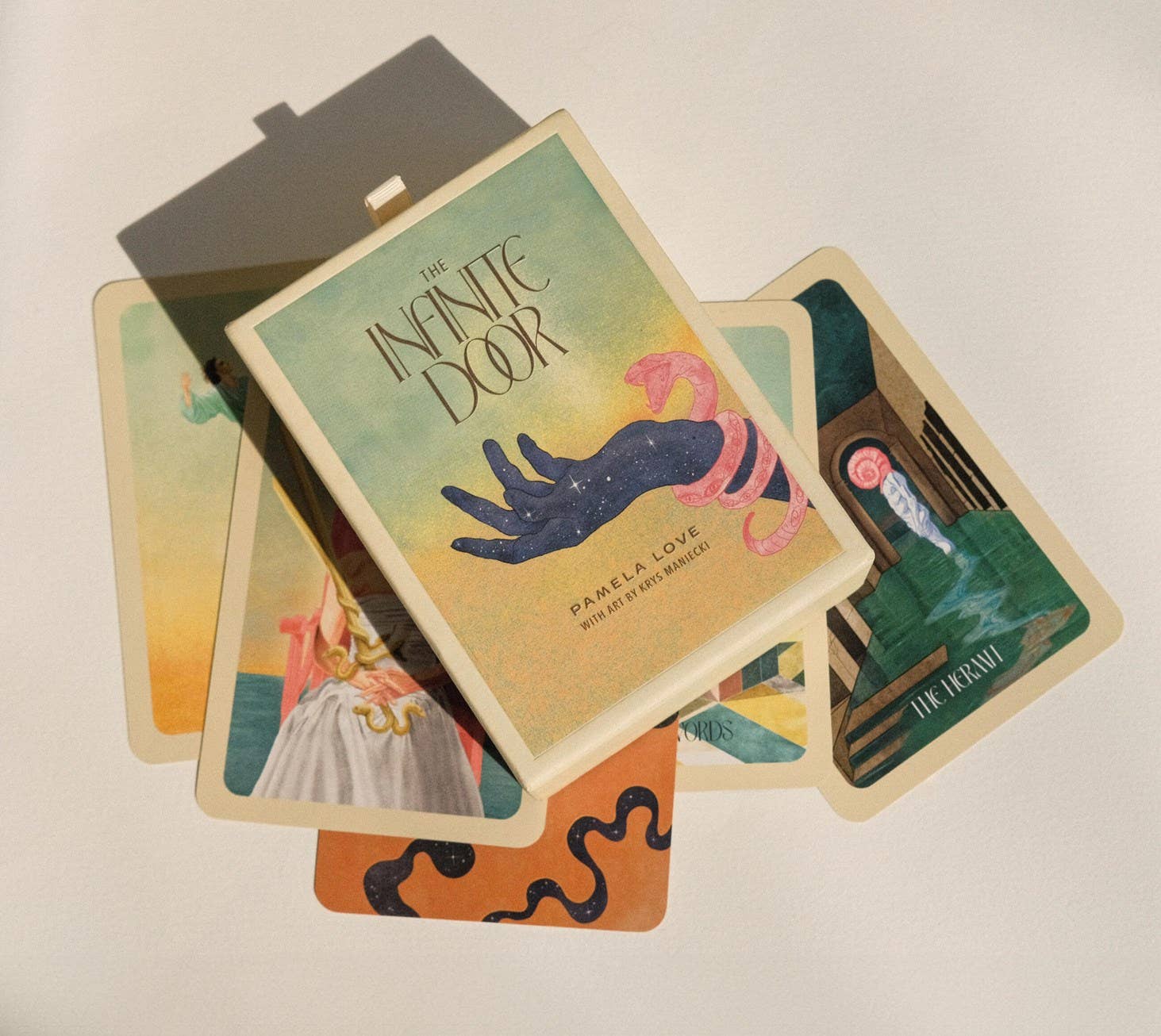 A fanned-out display of illustrated tarot cards from 'The Infinite Door' deck by Pamela Love, photographed on a plain light background with soft shadows.