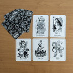 Set of black and white playing cards with intricate designs on a wooden surface.
