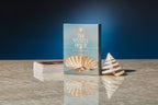 Book titled 'The Seashell Oracle' with two seashells on a reflective surface against a dark blue background