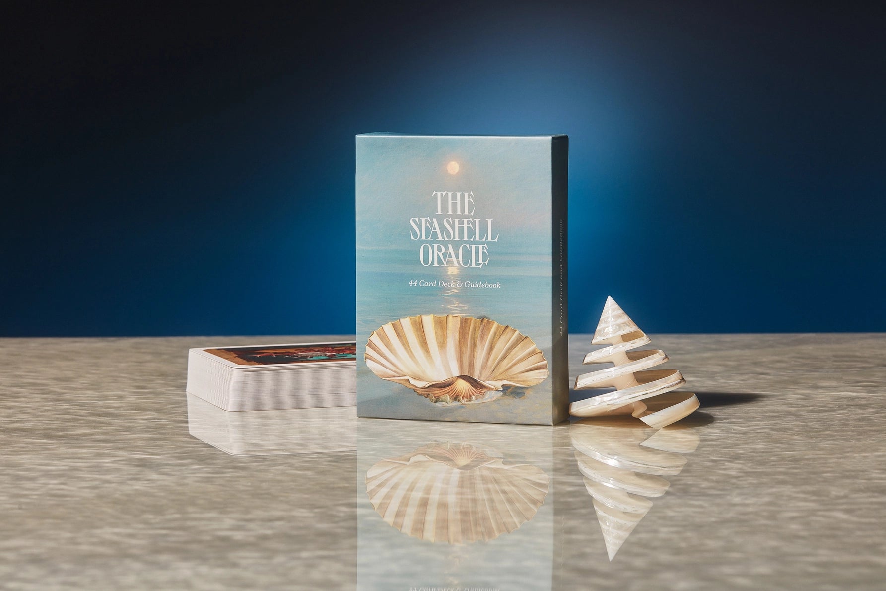 Book titled 'The Seashell Oracle' with two seashells on a reflective surface against a dark blue background