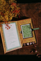 Decorative box with a green card and small items on a textured surface with flowers.