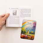 Hand holding an open book with a colorful card featuring a windmill and rainbow titled 'Clarity is on its way' on a white surface.
