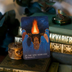 Tarot card titled 'The Nine Morgans' held by hands against a dark background with a fire and moon illustration.
