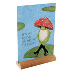 Card with a frog wearing a red mushroom hat on a blue background, featuring text 'It's so brave of me to exist.'