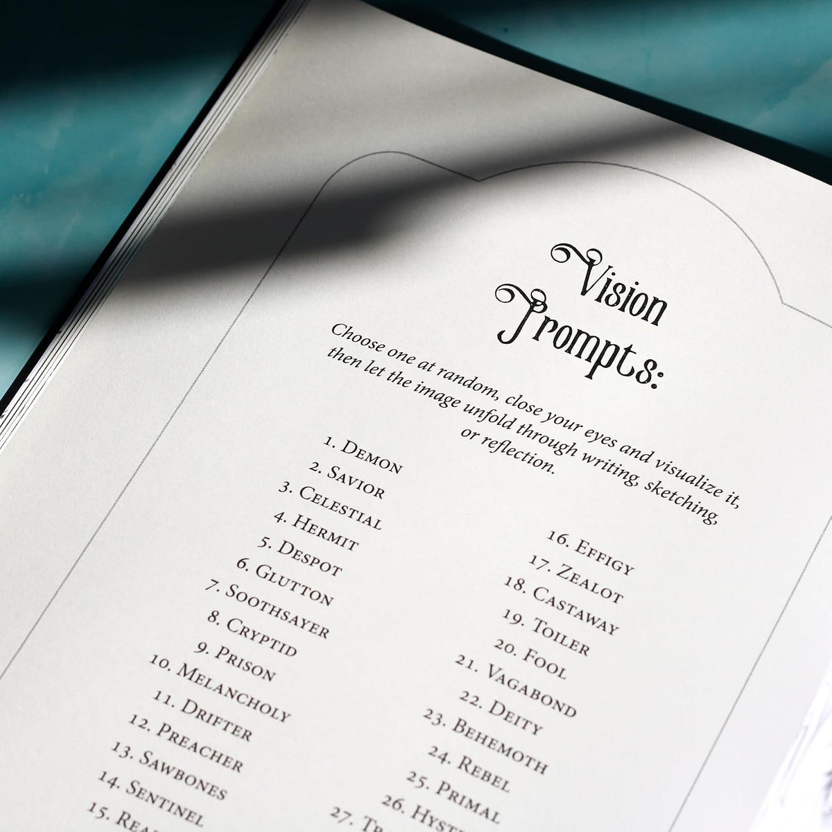 An open book or booklet showing a printed page titled 'Vision Prompts' with a list of numbered prompt words, photographed on a teal surface with a diagonal shadow across the page.