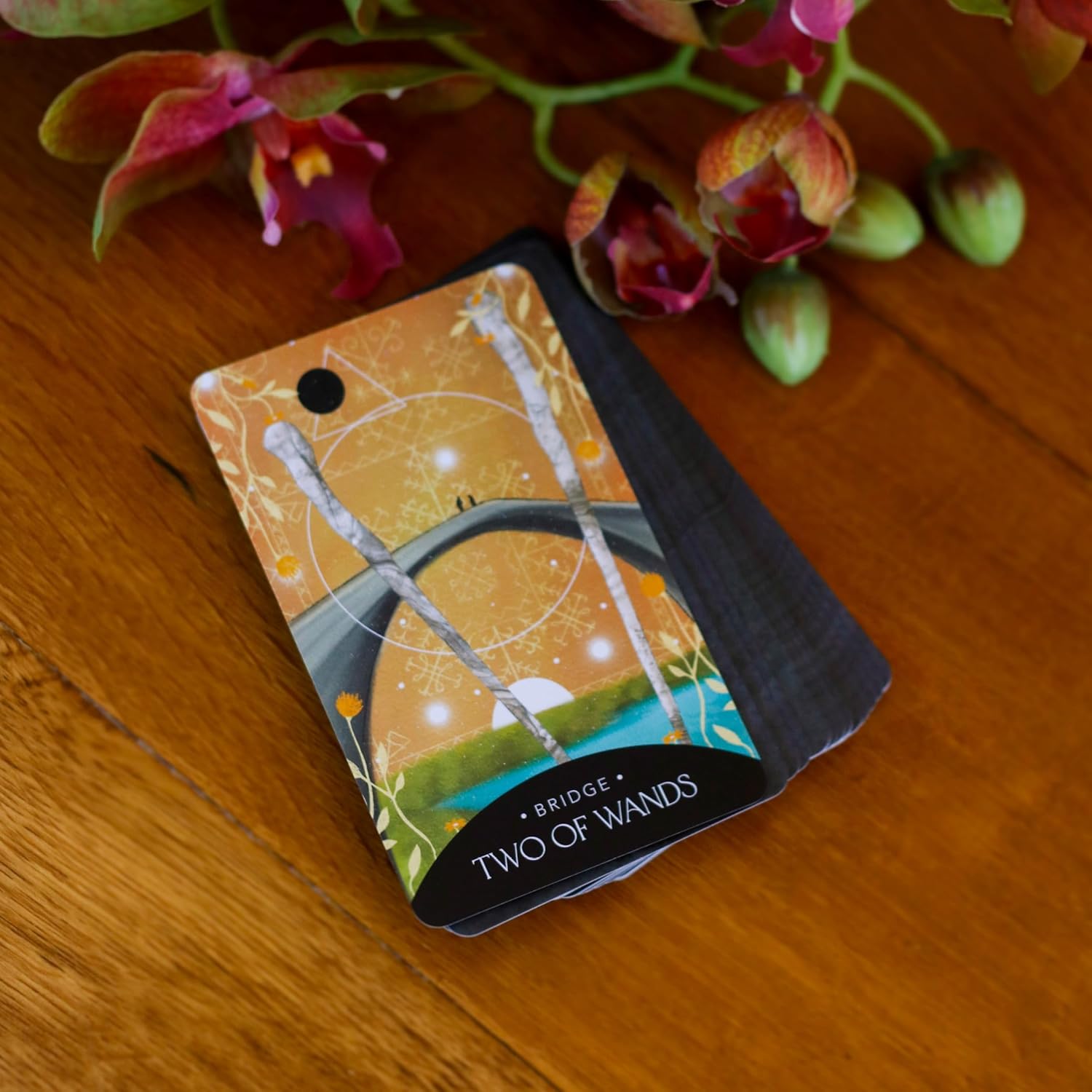 Two of Wands tarot card on a wooden surface with flowers in the background