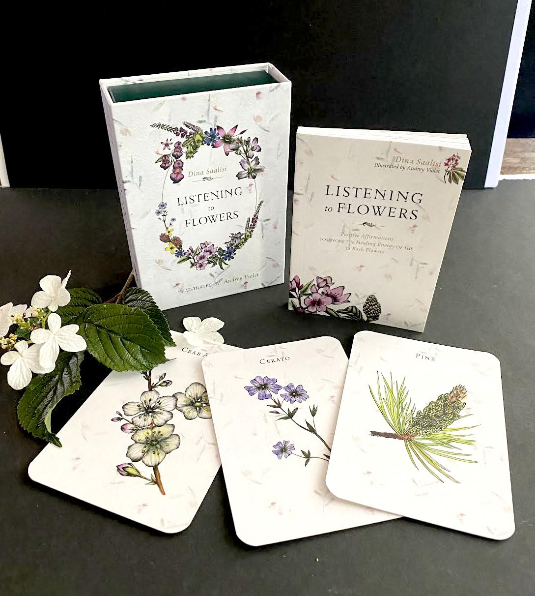 Books and card decks titled 'Listening to Flowers' on a dark surface with floral illustrations.