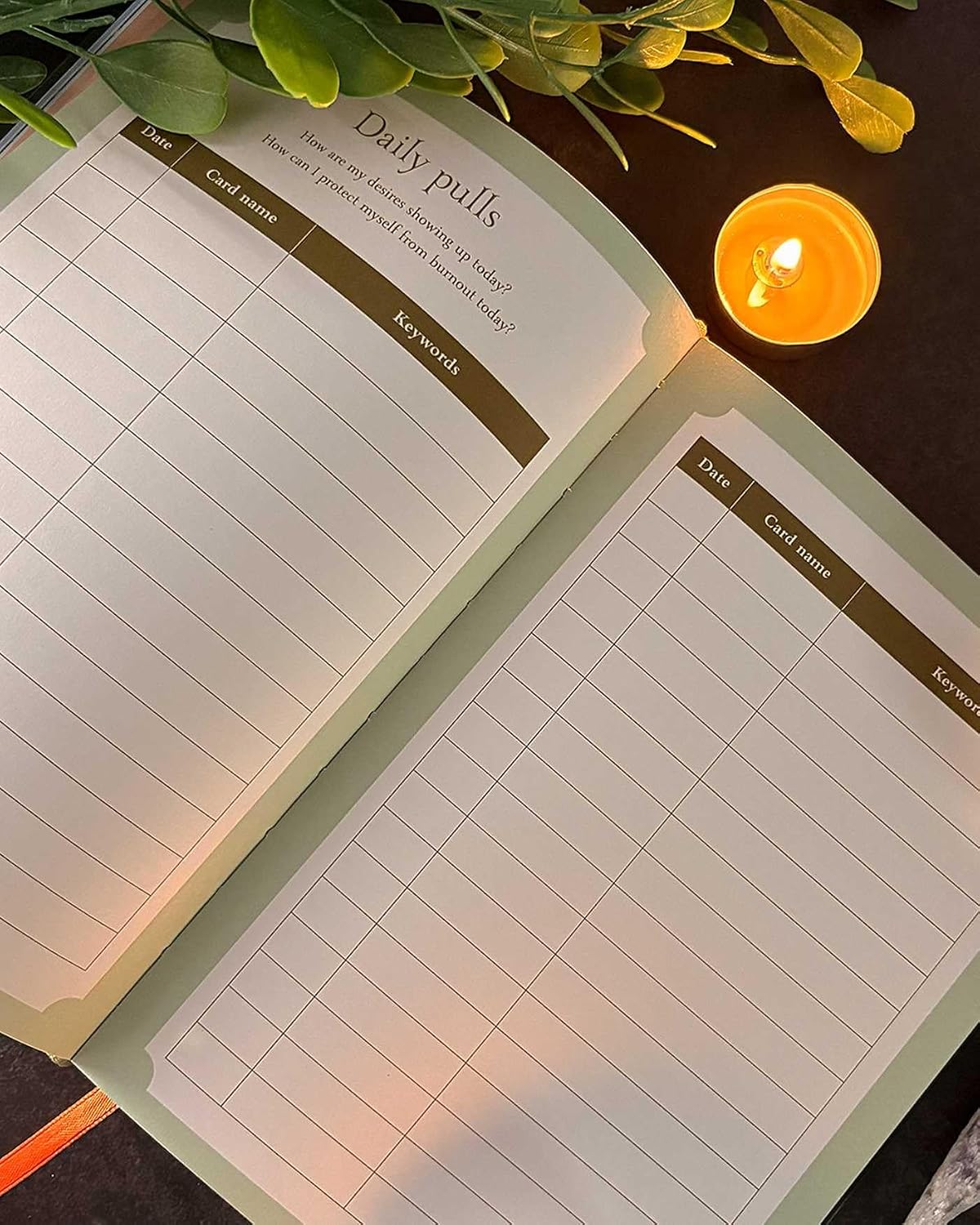 An open daily pull list notepad with lined pages and a header reading 'Daily pulls,' styled on a dark surface with green leaves and a lit candle nearby.