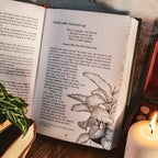 Open book with botanical illustration on a wooden surface with a candle