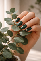 Hand with dark green nail polish holding a leafy branch