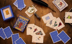 Playing cards with illustrations on a wooden surface, including a magnifying glass and feather quill.