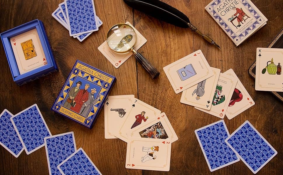 Playing cards with illustrations on a wooden surface, including a magnifying glass and feather quill.