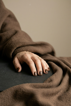 Hand with dark nail polish resting on a surface, wearing a brown garment.