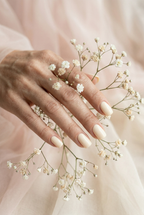 Hand with light manicure holding a small branch of white flowers against a soft pink background