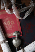 Decorative items including a red book with gold design, silver heart-shaped object, and white ribbons on a dark surface.