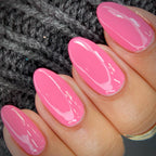 A close-up of a hand with long, glossy pink manicured nails resting against a dark gray knitted background.