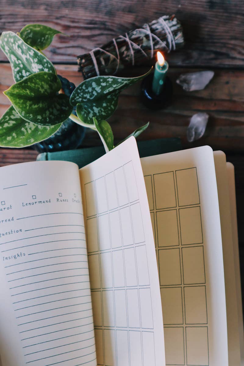 Open notebook with lined and grid pages on a wooden surface with a plant and candle.