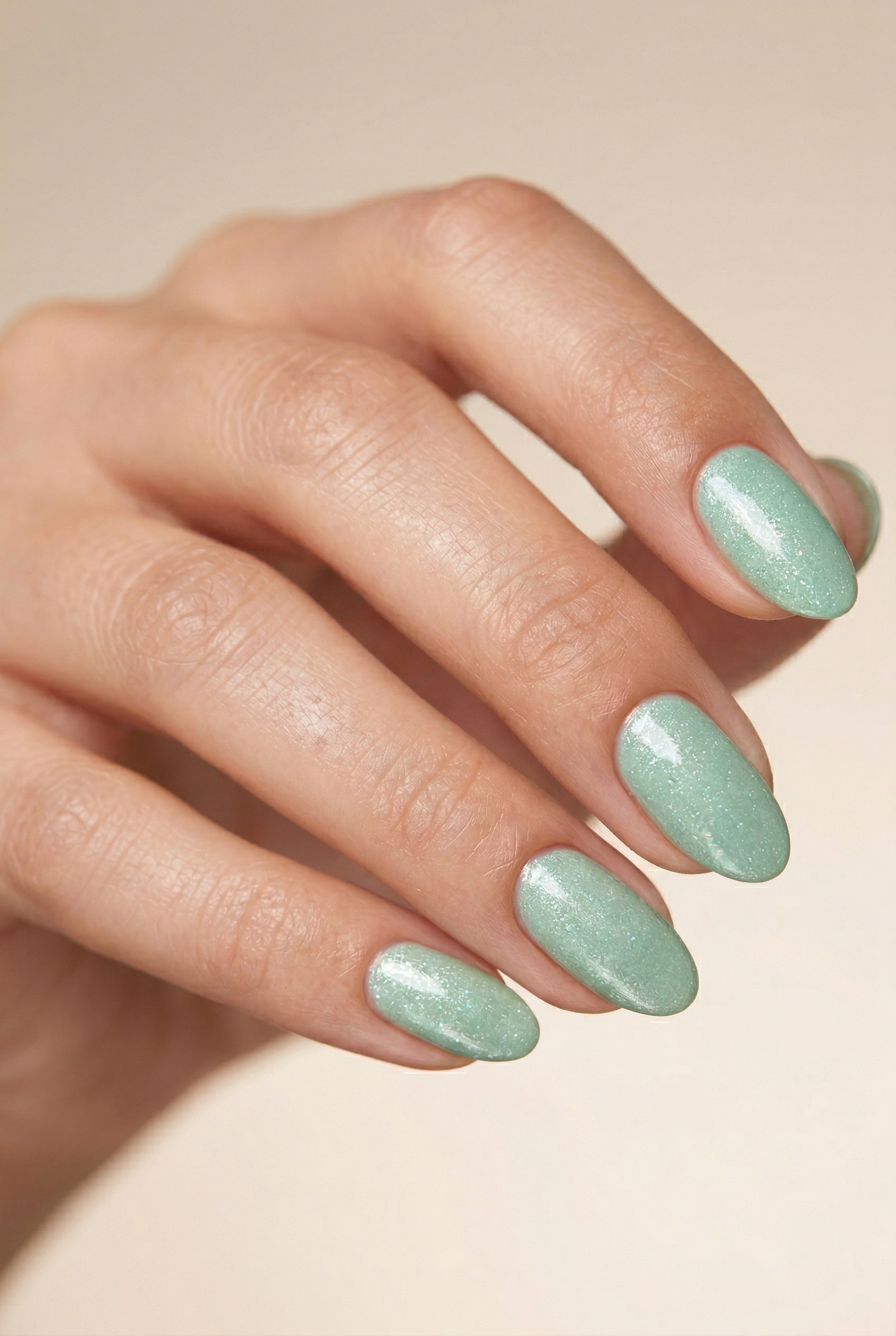 Hand with light green nail polish on a beige background