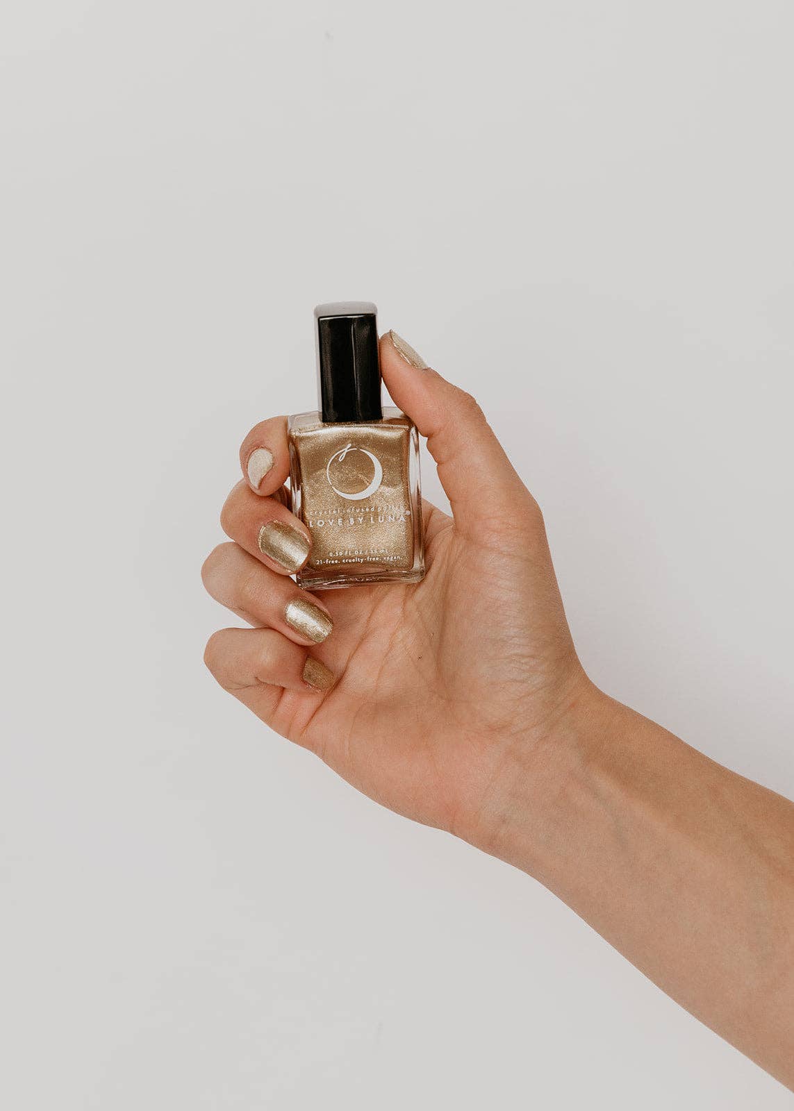 Hand holding a small bottle of nail polish against a plain background
