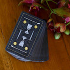 Stack of tarot cards with symbolic designs on a wooden surface with flowers.