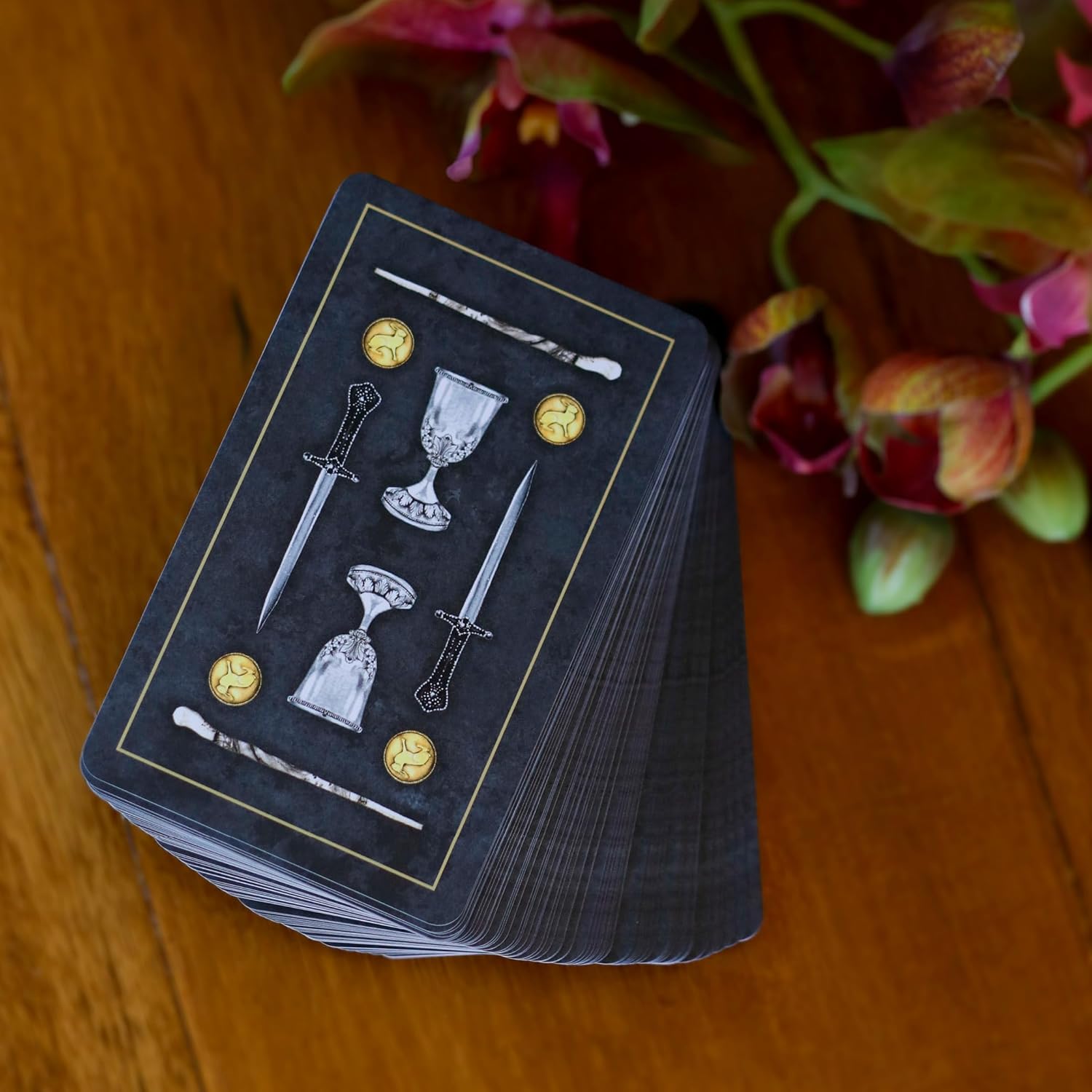 Stack of tarot cards with symbolic designs on a wooden surface with flowers.