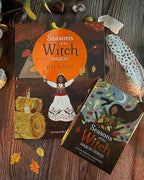 Two books titled 'Seasons of the Witch' on a wooden surface with autumn leaves and candles.