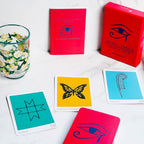 Red Oracle Deck with cards featuring symbols and a glass with floral design on a white surface.