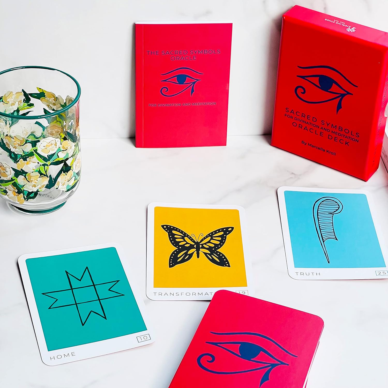Red Oracle Deck with cards featuring symbols and a glass with floral design on a white surface.