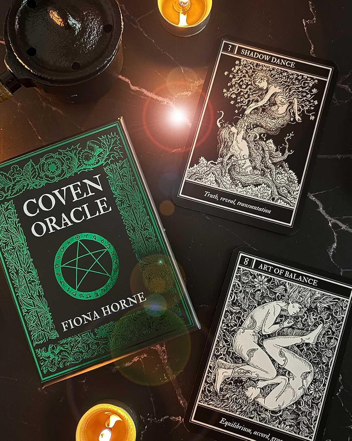 Coven Oracle book by Fiona Horne with tarot cards on a dark surface with candles.