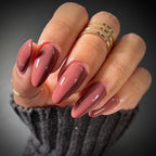 Hand with pink nail polish and gold rings on a dark background