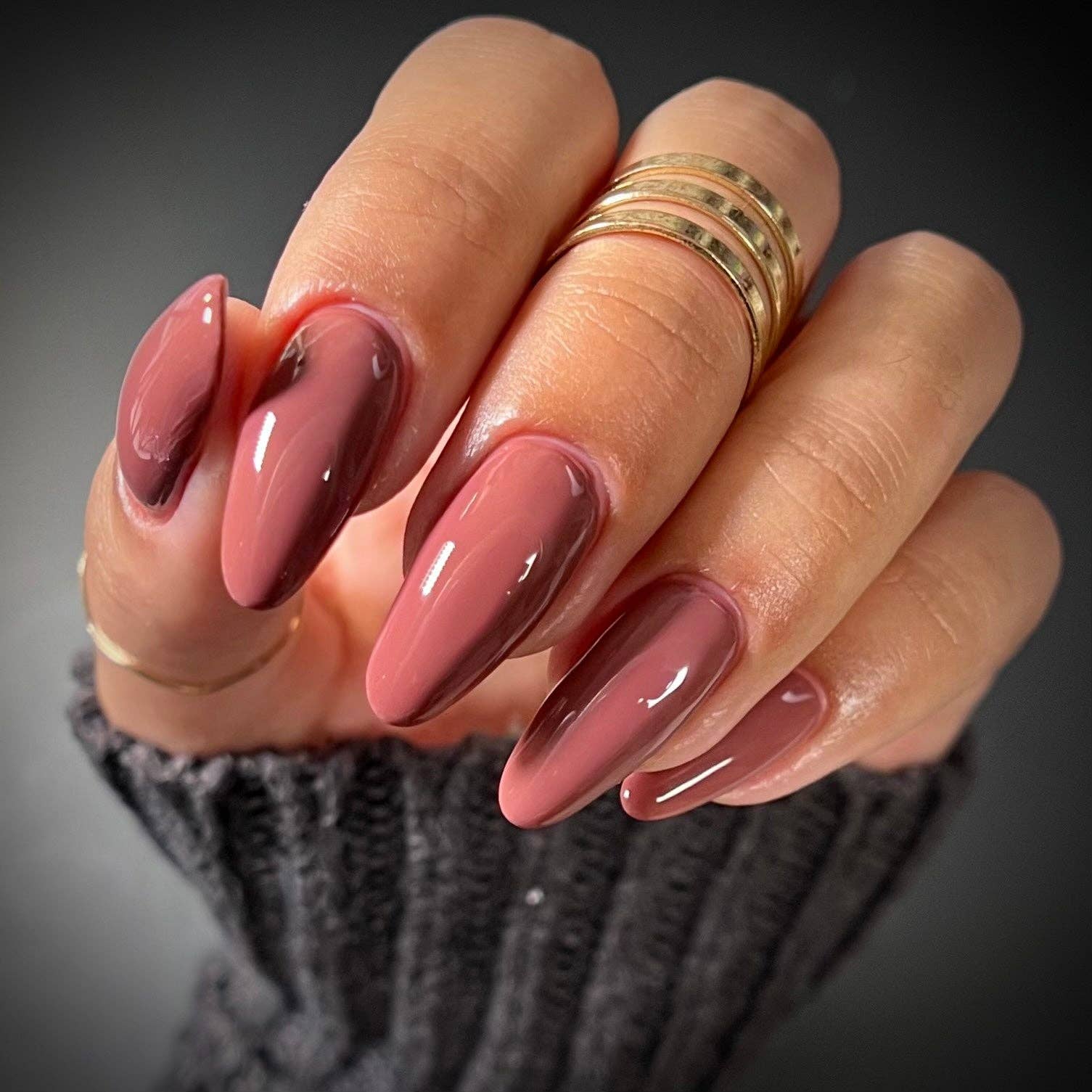 Hand with pink nail polish and gold rings on a dark background