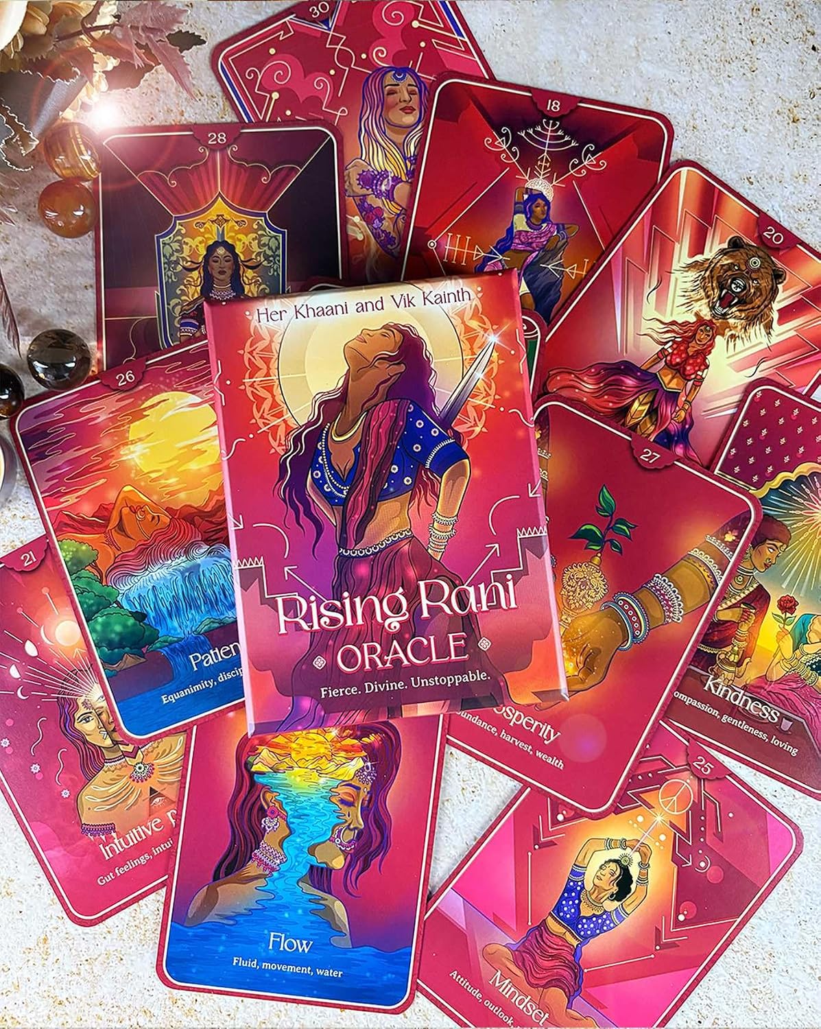 A spread of colorful oracle cards from the Rising Rani Oracle deck, featuring vibrant illustrations and titles such as Patience, Flow, and Karma, arranged on a light textured surface.