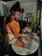 Woman in an orange shirt looking at tarot cards on a table in a cozy room with plants and books.